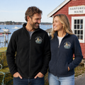 The Titsy Mermaid embroidered Columbia fleece jacket in black and navy by a Maine coastal harbor
